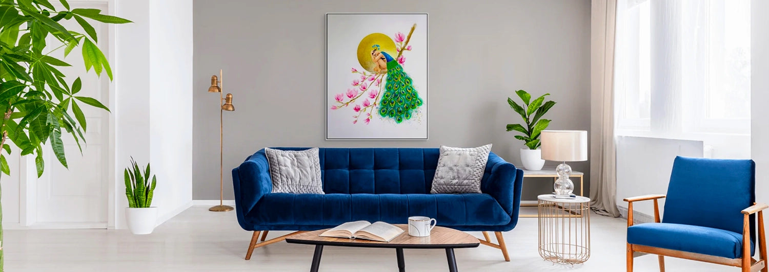 Bright lounge with blue velvet couch, arm chair and framed print of peacock-like woman on magnolia branch in the background.