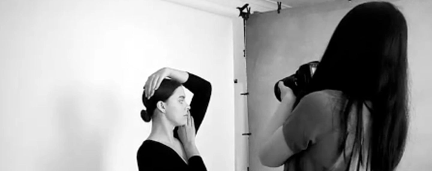 A black and white behind the scenes image of a photographer taking a photo of a model.