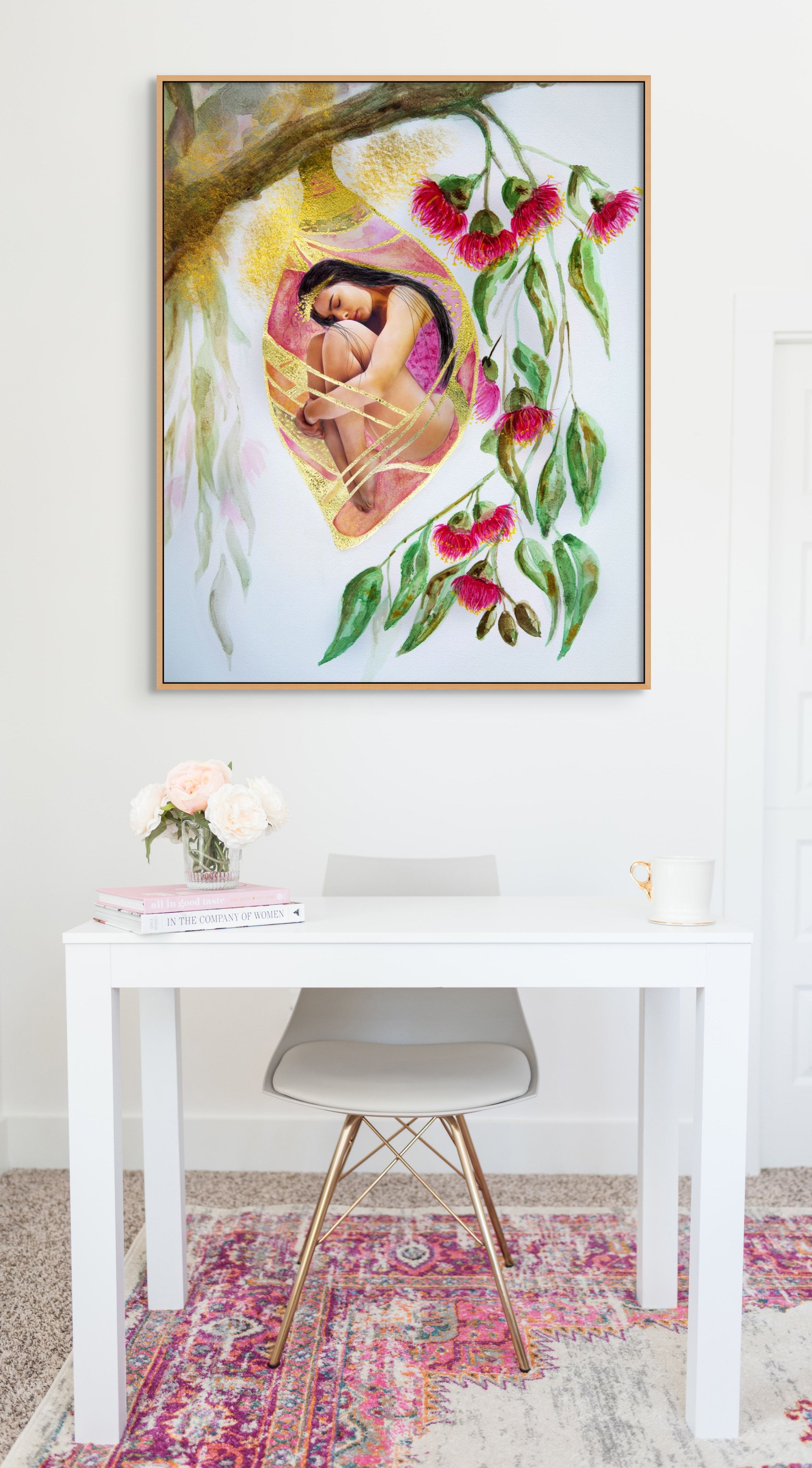 White office desk and chair with a framed Hue the Artist art print above: a woman in a cocoon hanging from a branch with pink gum nut flowers.