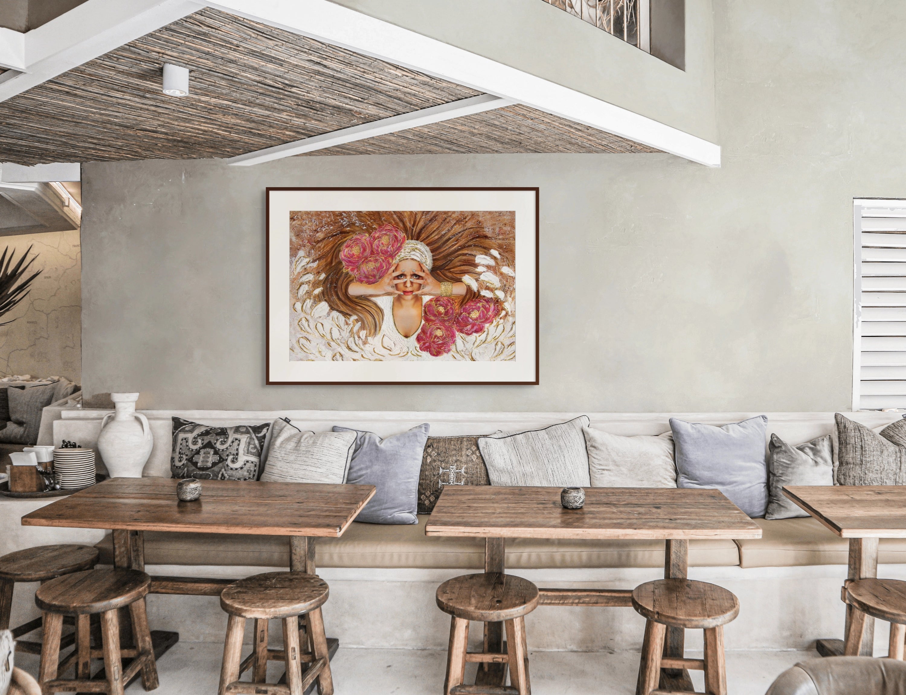 Boho-style café with wooden beige furniture, featuring large Hue the Artist framed art print of a woman with brown hair, magenta flowers, and gold petals.