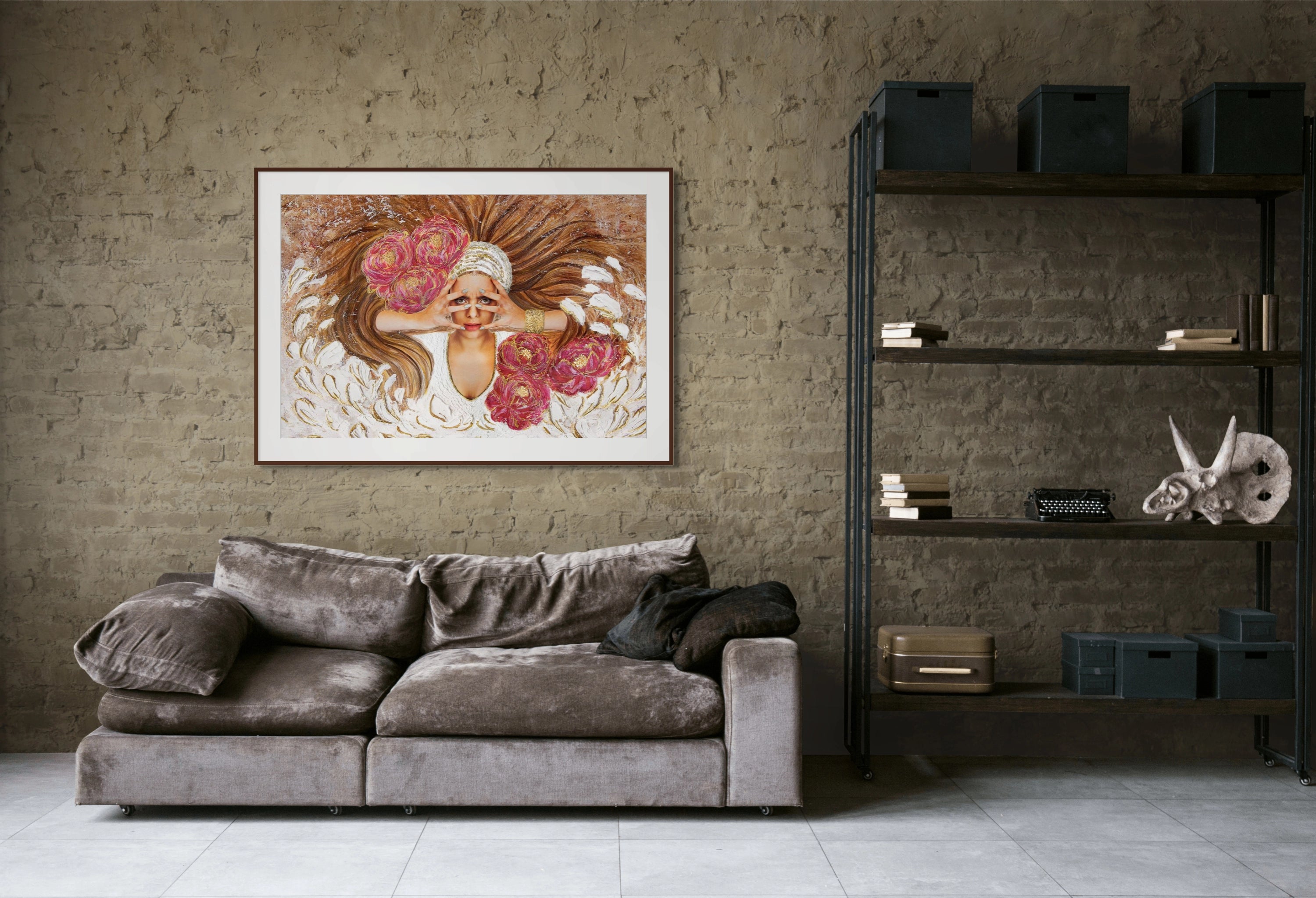 Beige room with brick wall, industrial bookcase, and brown velvet couch. Above it is a large Hue the Artist framed print of woman with her hand over her face, wild brown hair and magenta flowers.