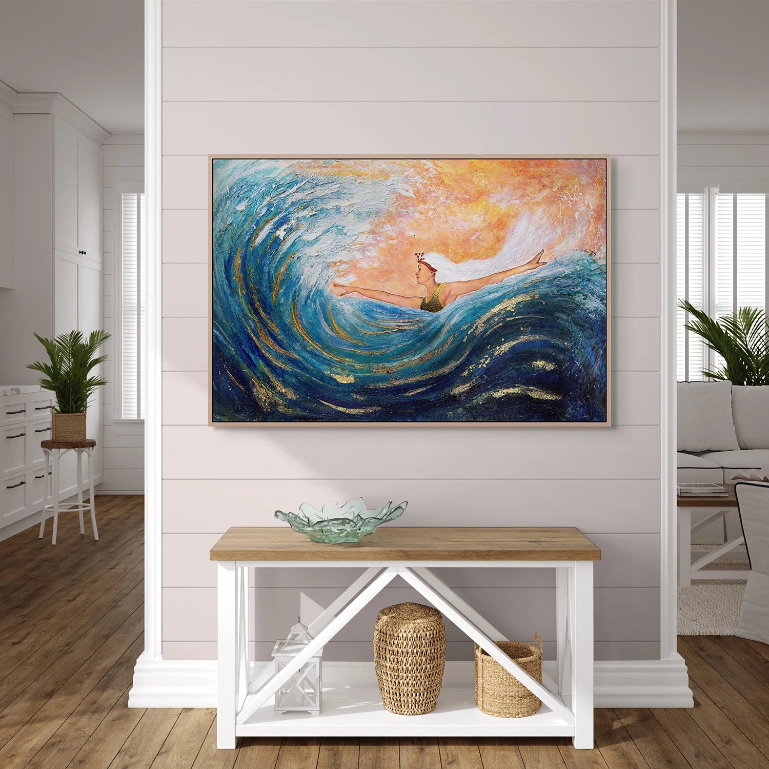 Entry wall with a white decorative table below a large blue and orange framed print by Hue the Artist of a woman with arms wide, surfing a big wave.