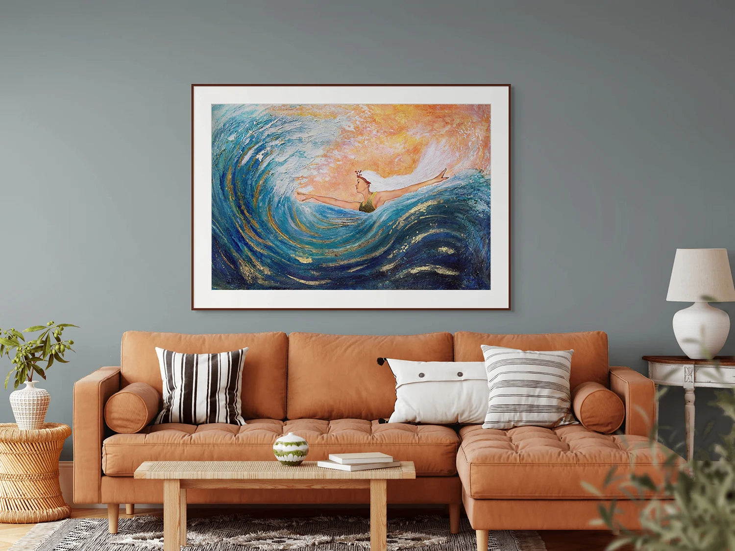 Hue the Artist mixed media print in a living room with a comfortable orange long below a large blue and orange framed print of a woman with arms wide, surfing a big wave.