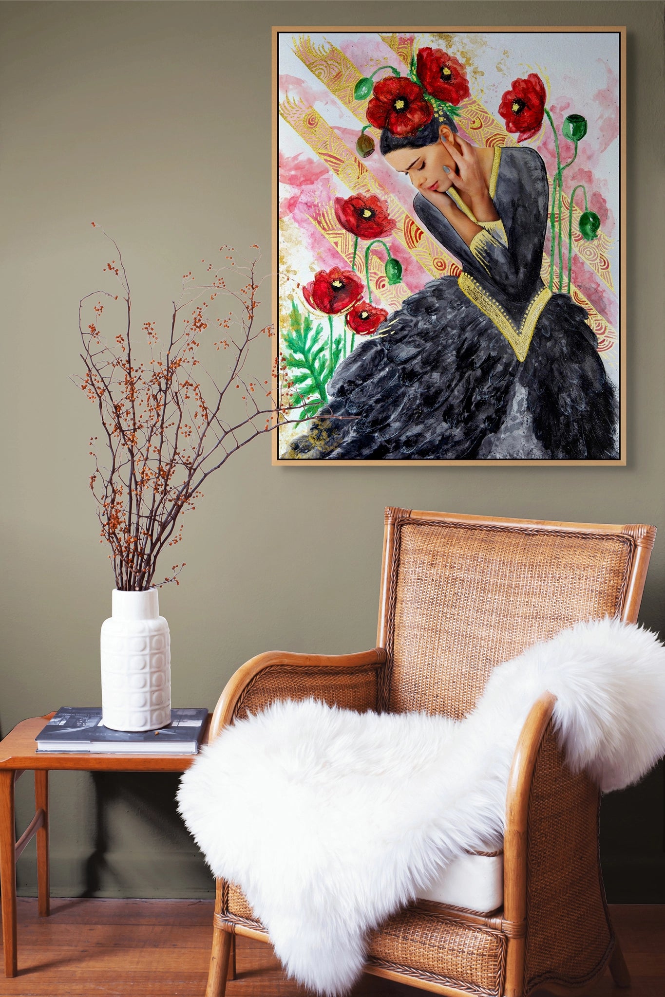 Famed art print by Hue the Artist of a sad woman with black and red poppies hangs above a wicker chair with a white rug and a white vase with twigs and berries.