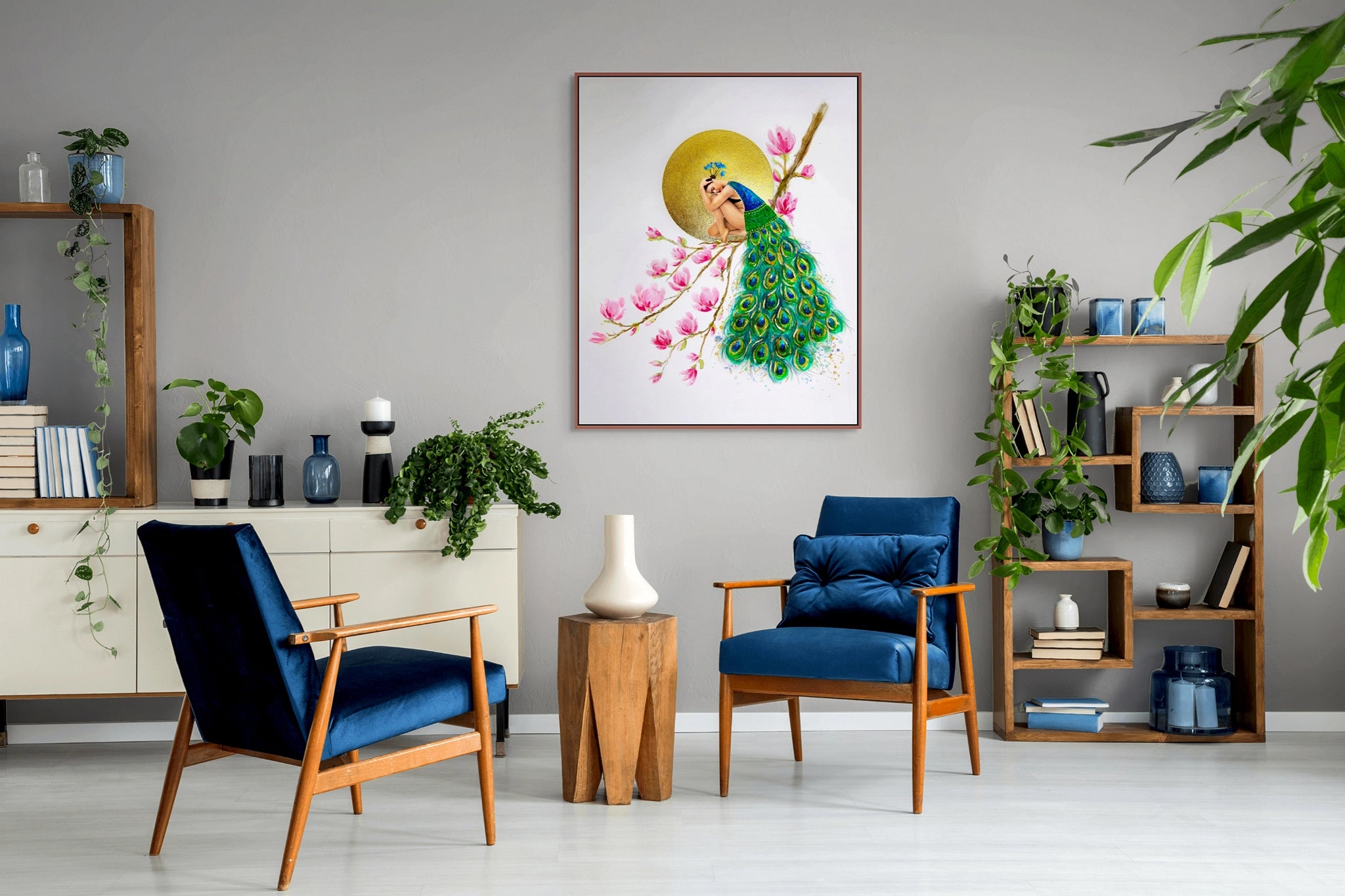 Hue the Artist canvas print of woman in a peacock feather cloak, hangs in a room with two velvet blue chairs, decorative book case and indoor plants.