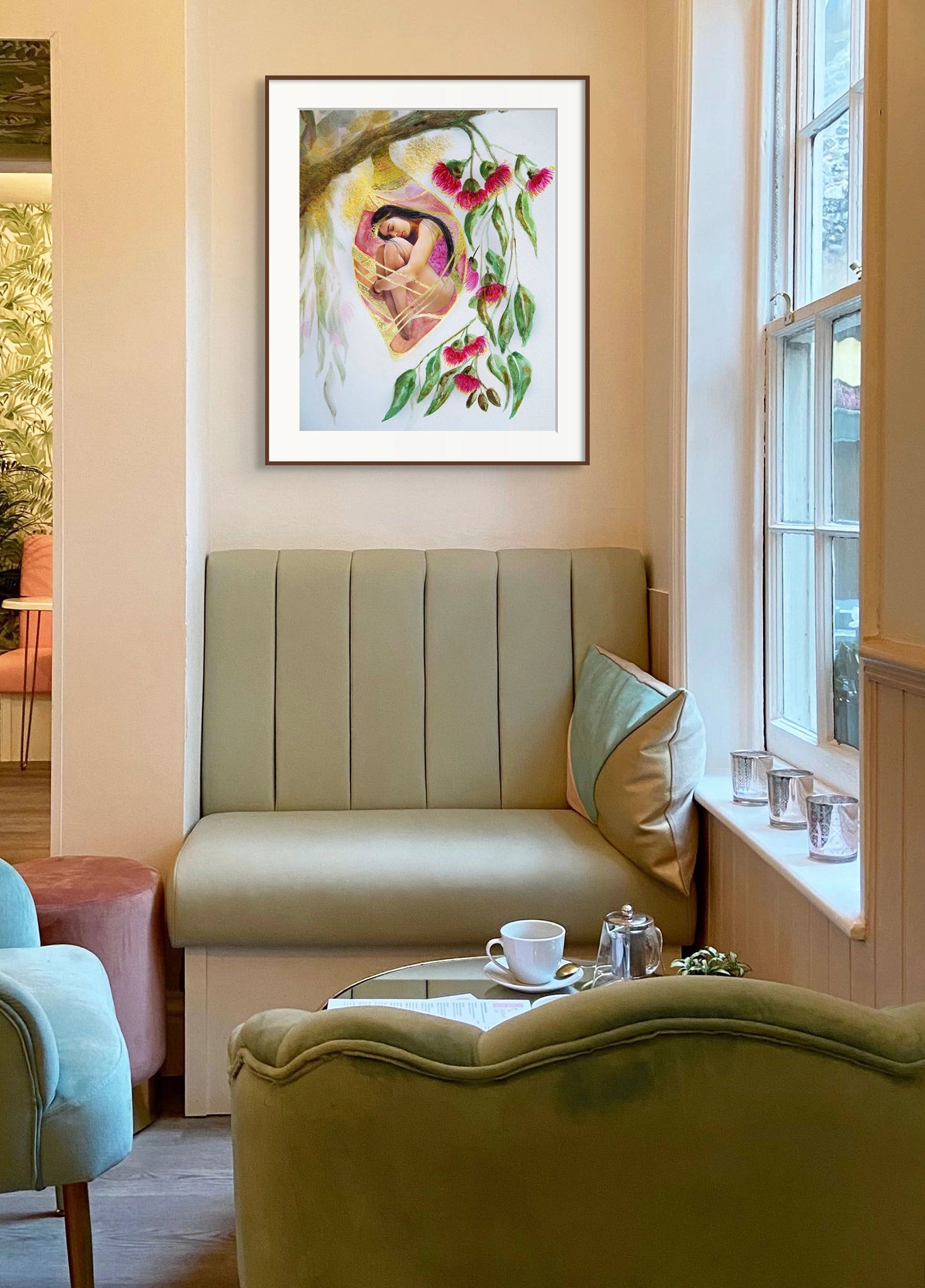 Framed Hue the Artist art print of woman in cocoon with pink gum nut flowers, hangs in cafe, above sage green leather booths.