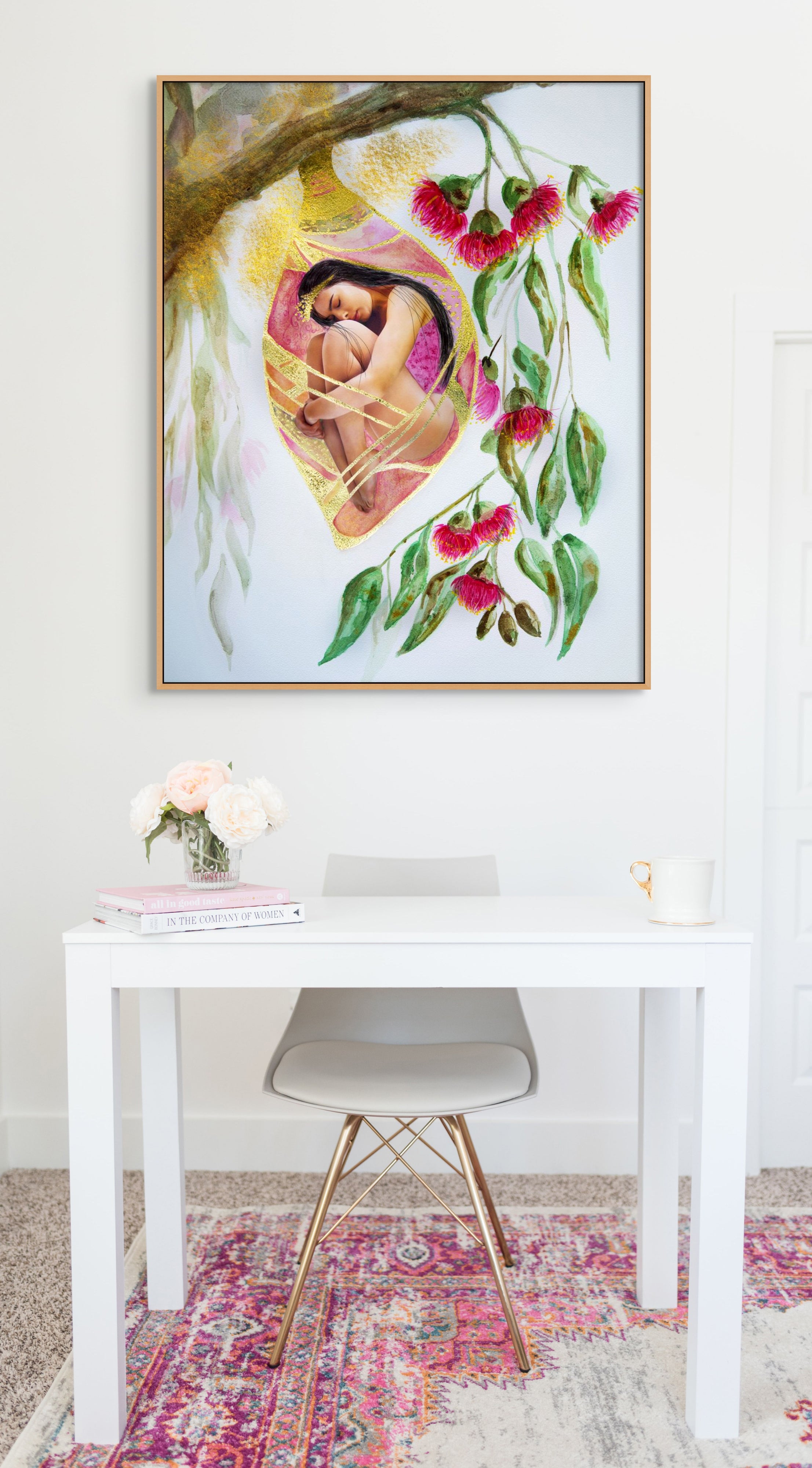 White office desk and chair with a framed Hue the Artist art print above: a woman in a cocoon hanging from a branch with pink gum nut flowers. 