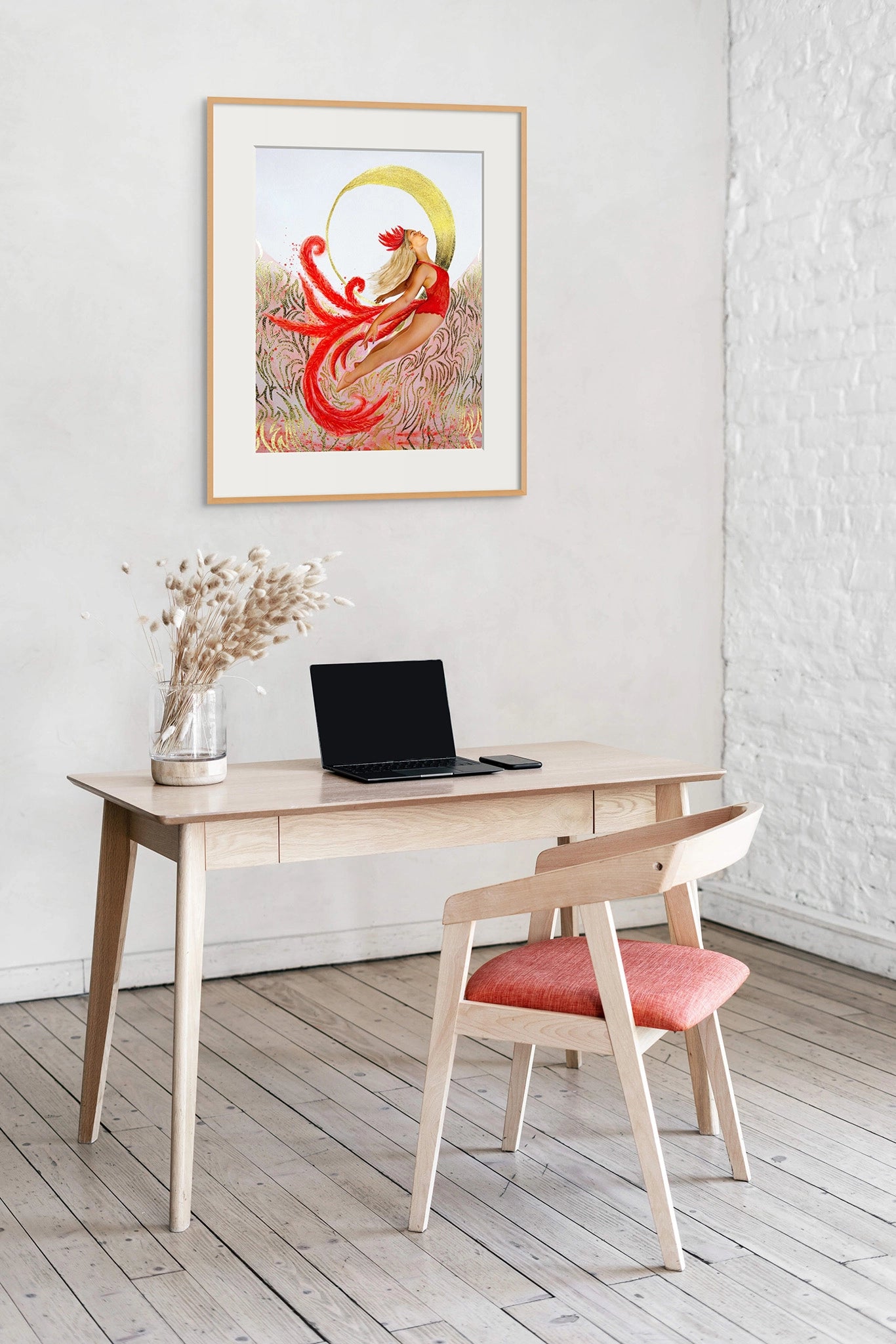 Framed Hue the Artist art print of an empowered woman in red flying up to a crescent moon hangs above a wooden office desk with a laptop, vase and red chair.