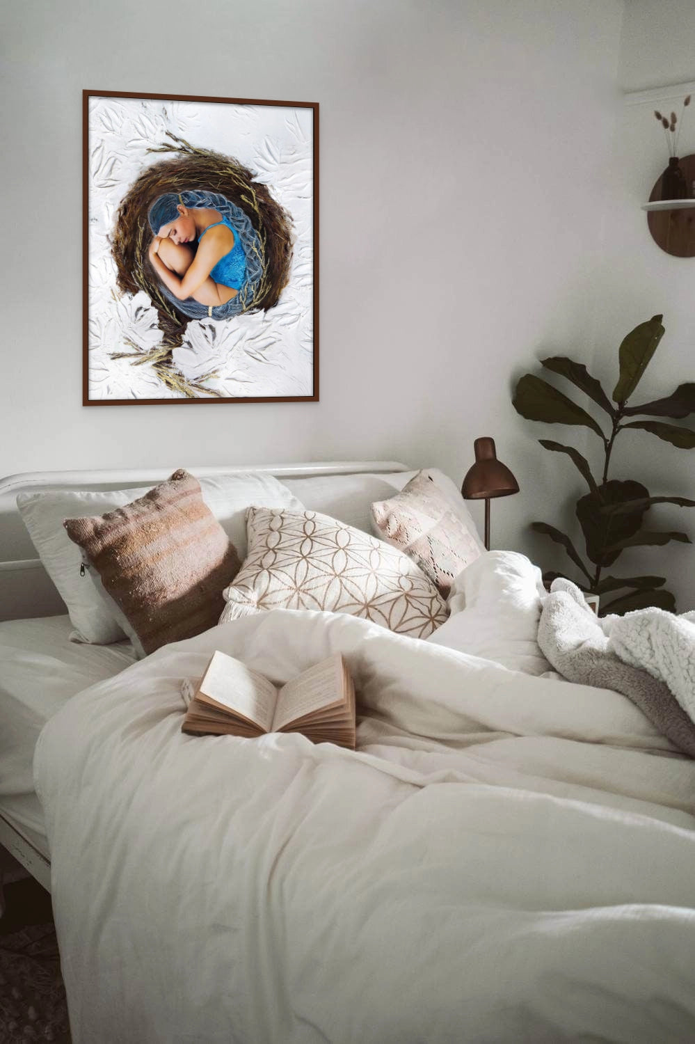 Large framed Hue the Artist art print of a woman with blue hair curled inside a birds nest hangs above a single bed with brown and cream cushions, plant and open book.