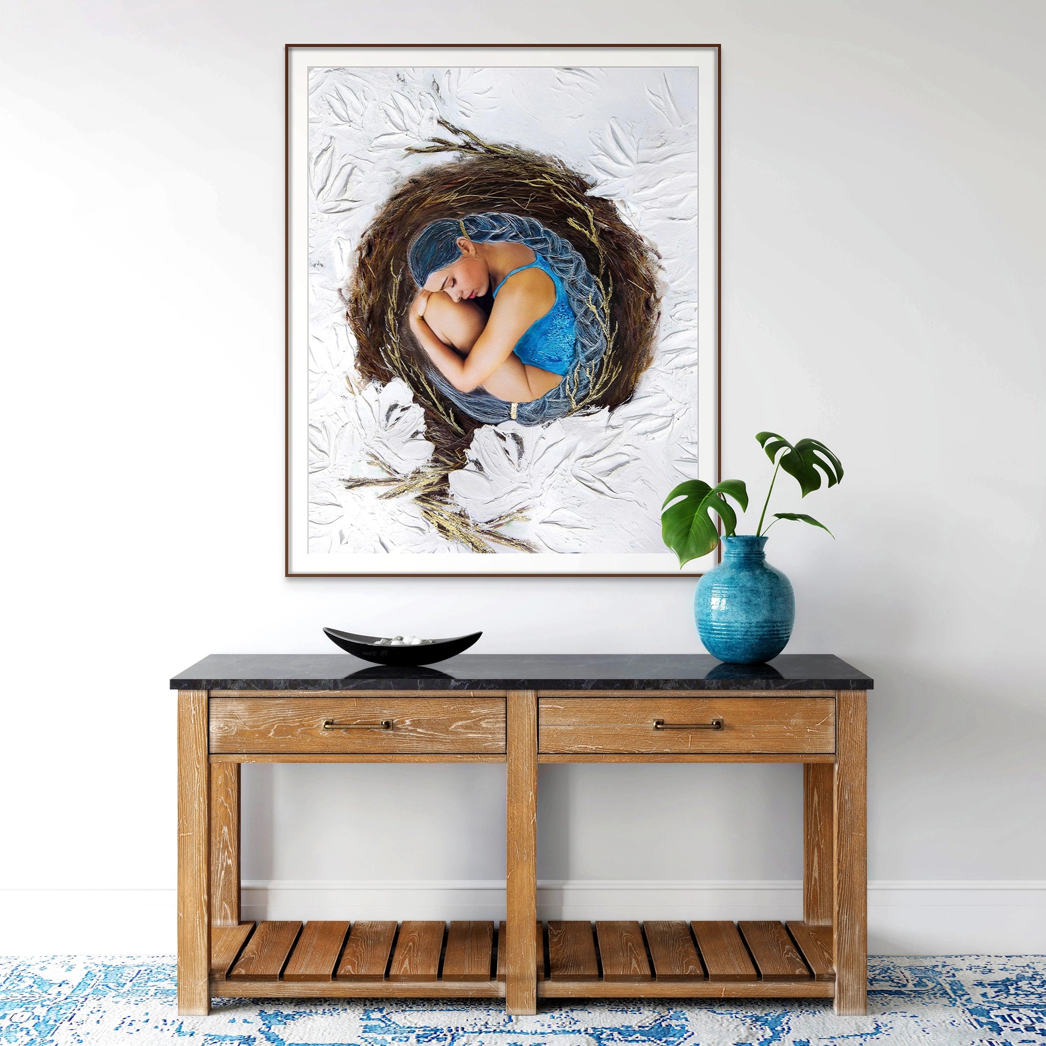 Large framed Hue the Artist artwork of a woman with blue hair curled inside a bird's nest. It hangs above a wood hall table with black marble top.