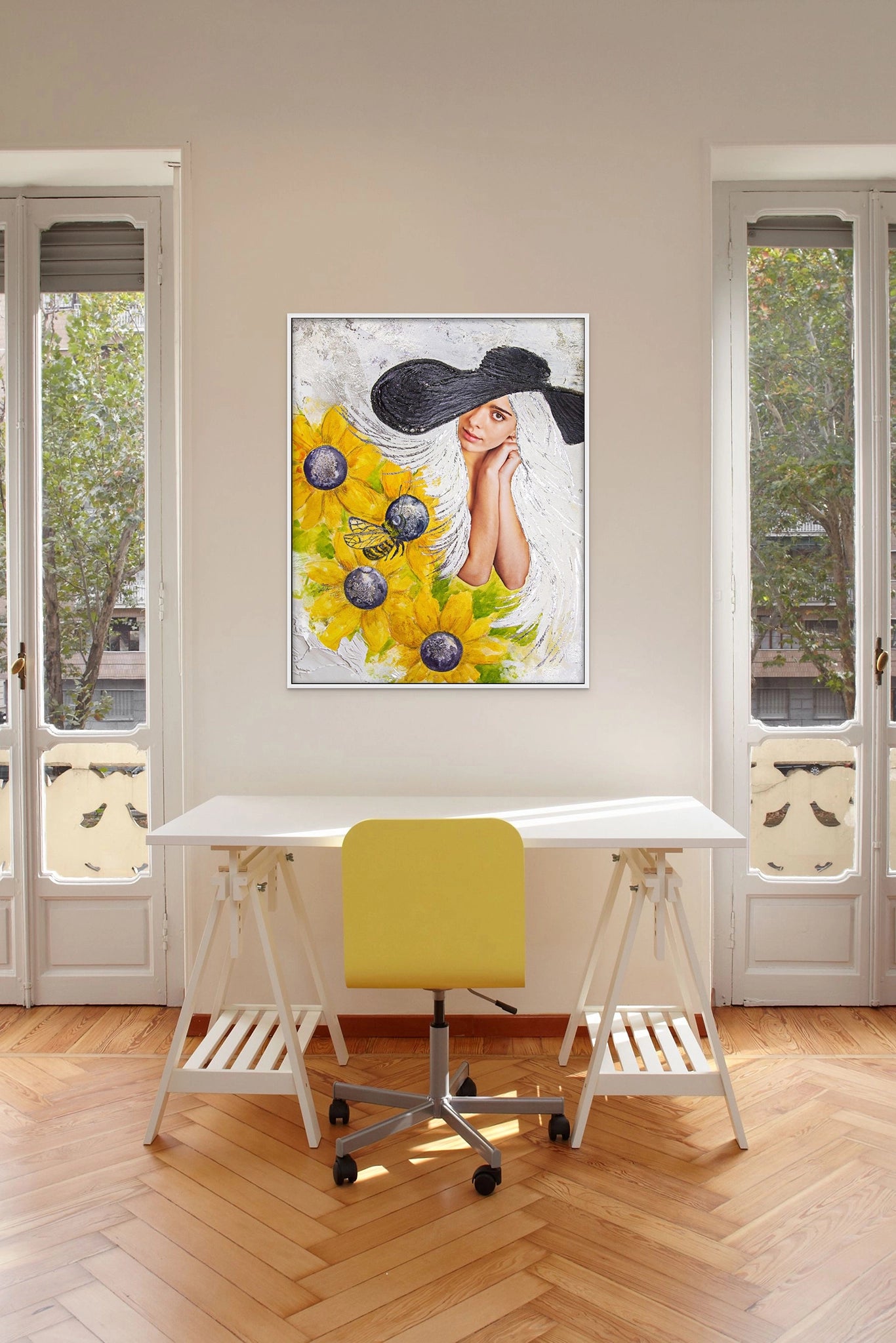 Hue the Artist framed art print of a white-haired woman in a black floppy hat with sunflowers hangs in a light-filled office with French doors, a desk, herringbone wood floors, and yellow chairs.