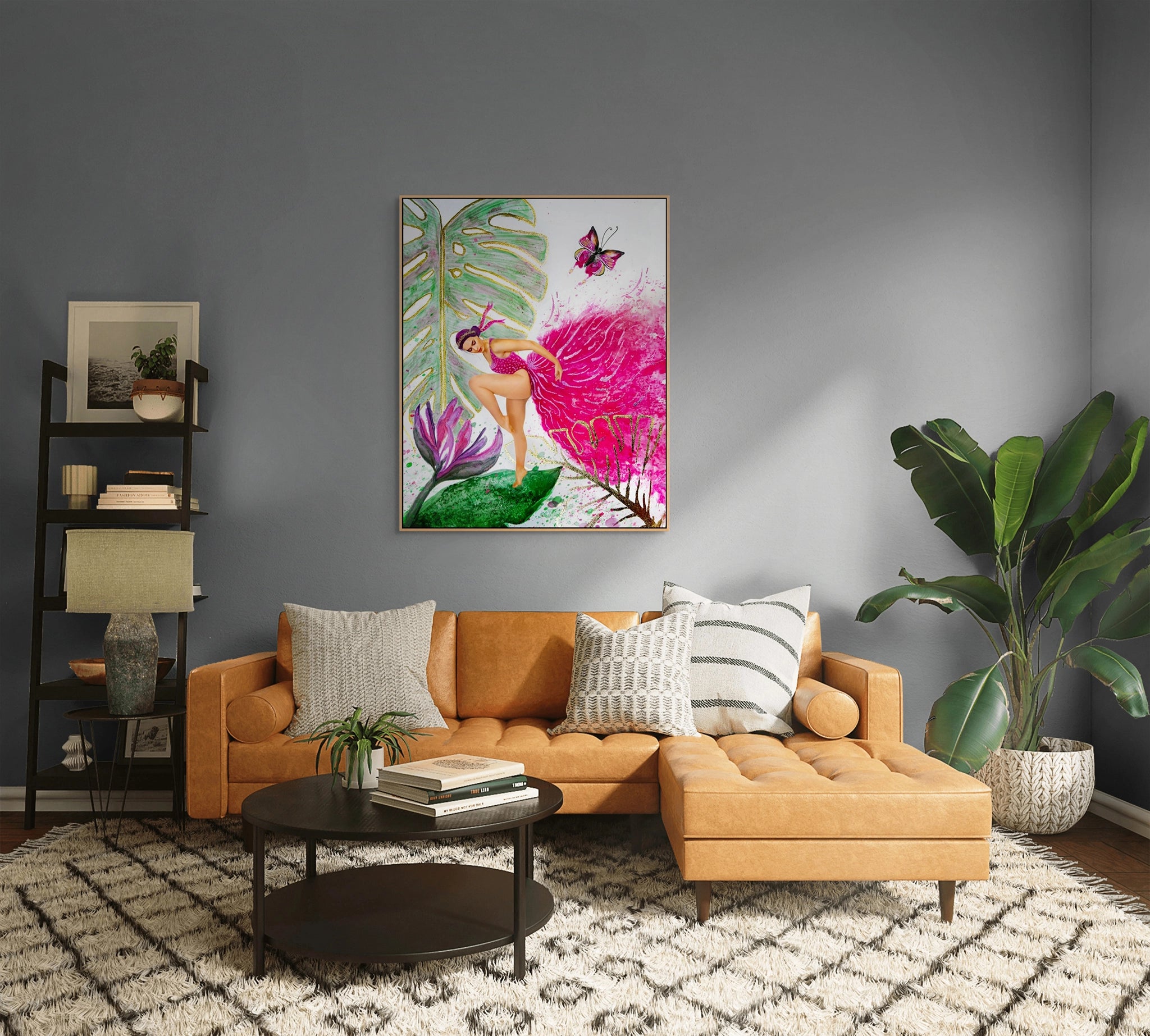 Hue the Artist framed canvas print of a woman in a bright pink gown hangs above a caramel couch. The room also has a large rug, a small bookcase, and an indoor plant.