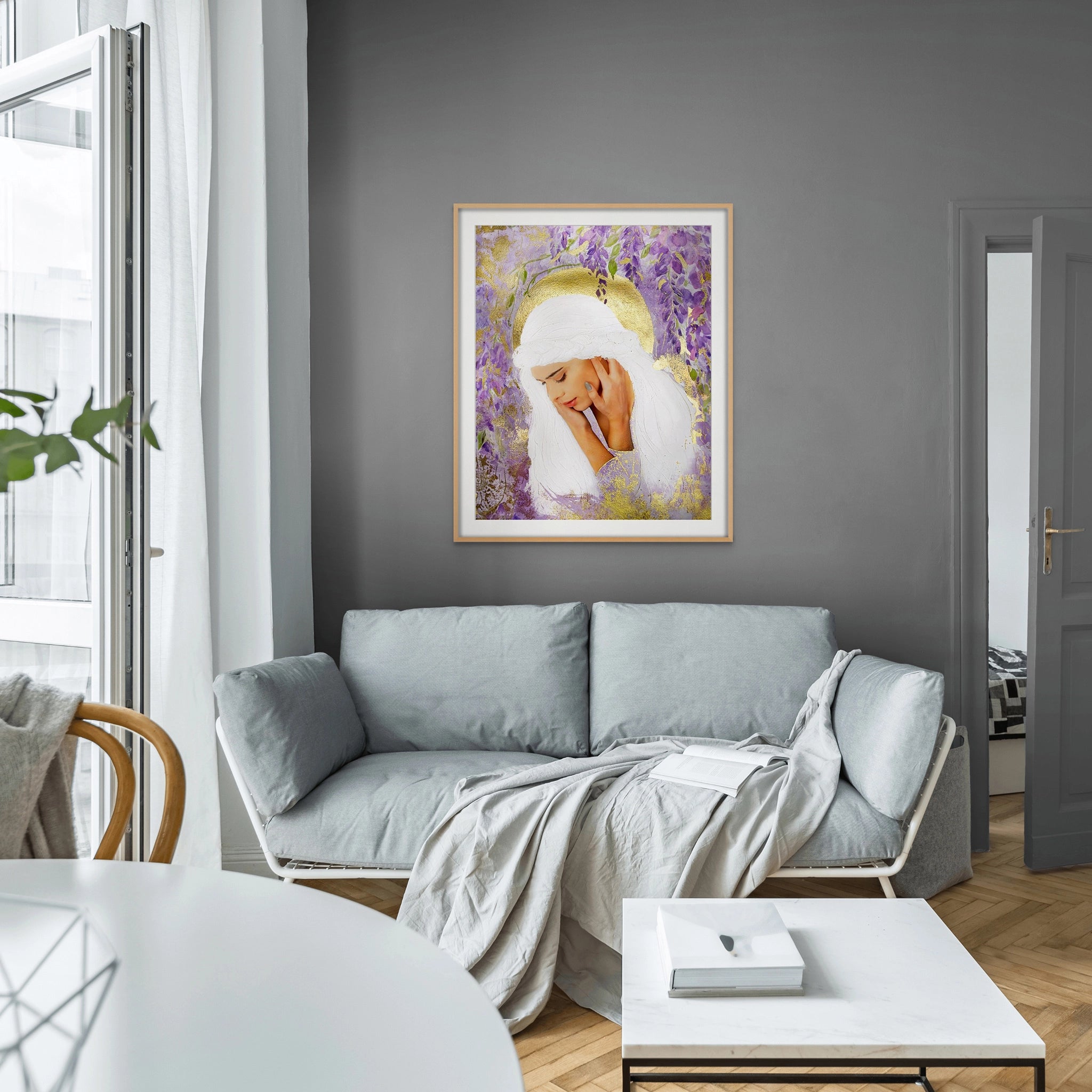 Framed Hue the Artist art print of a sad white haired woman, surrounded by purple wisteria and gold foil details hangs above a grey lounge in a light filled room.